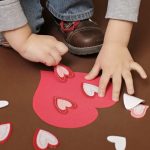 A preschooler has cut out multiple heart shapes in order to create a large heart made up of 3D hearts for Valentine's Day.