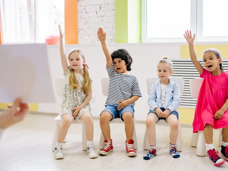 Students raise their hand to answer a teacher's question. Image complements the blog: Transitional Kindergarten TK vs. Pre K.
