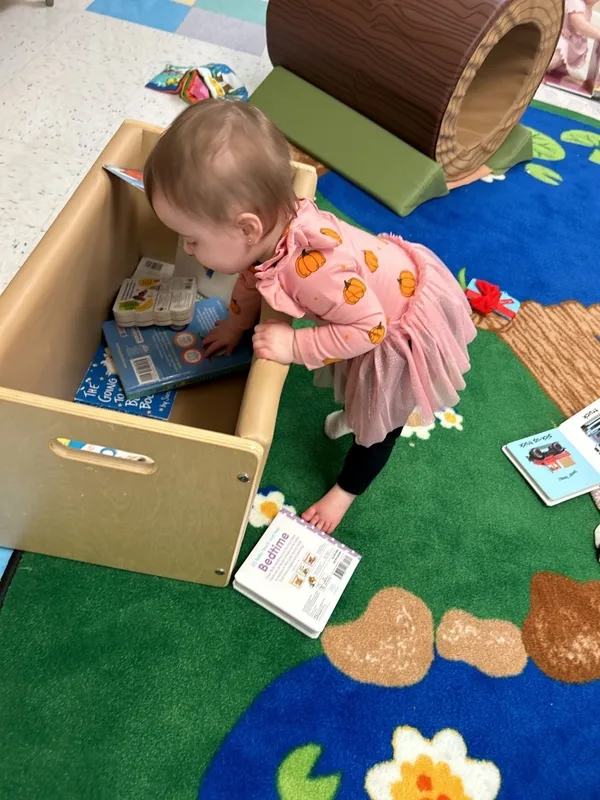 Toddler looking in book bin. This image accompanies the blog exploring daycare vs preschool. 