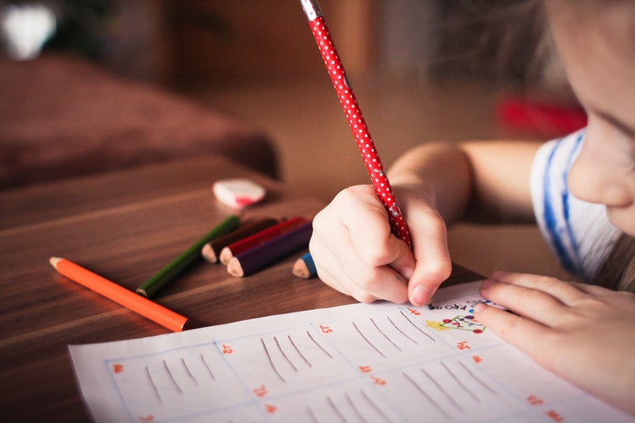 A young girl is practicing writing skills using a pencil. This image is intended to be the featured image for the blog post titled, The Importance of Handwriting for Preschoolers."