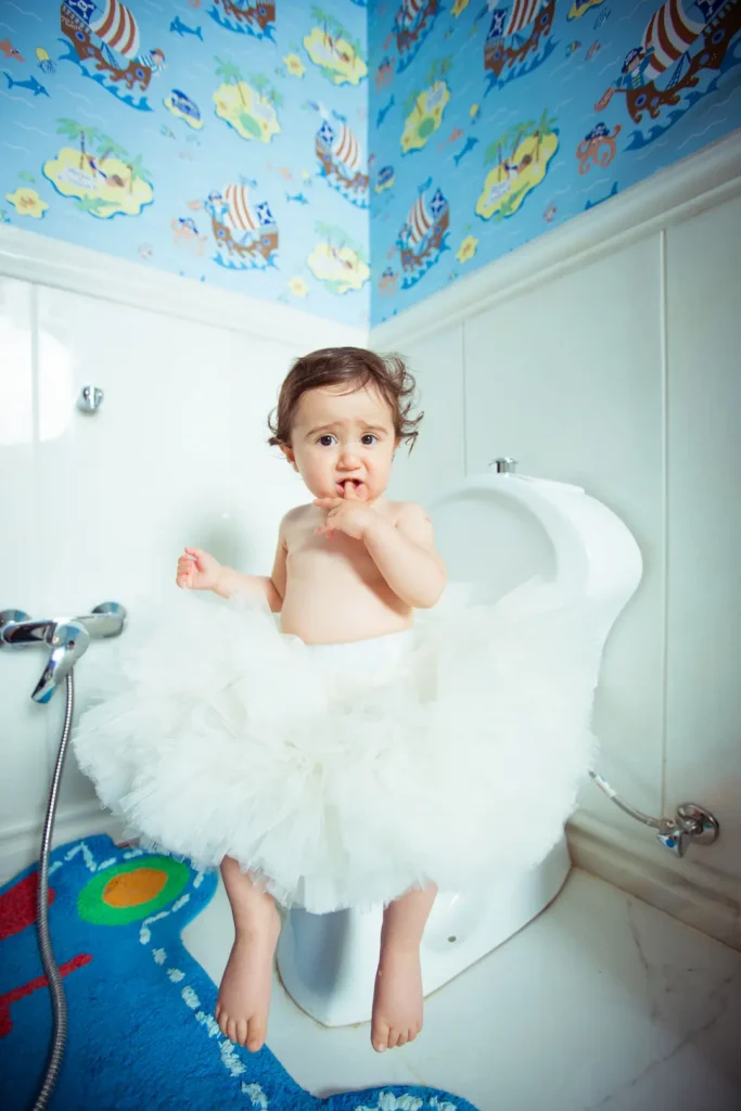 baby in white tutu sitting on a toilet seat in colorful bathroom. Image complements the blog: how to potty train child for daycare