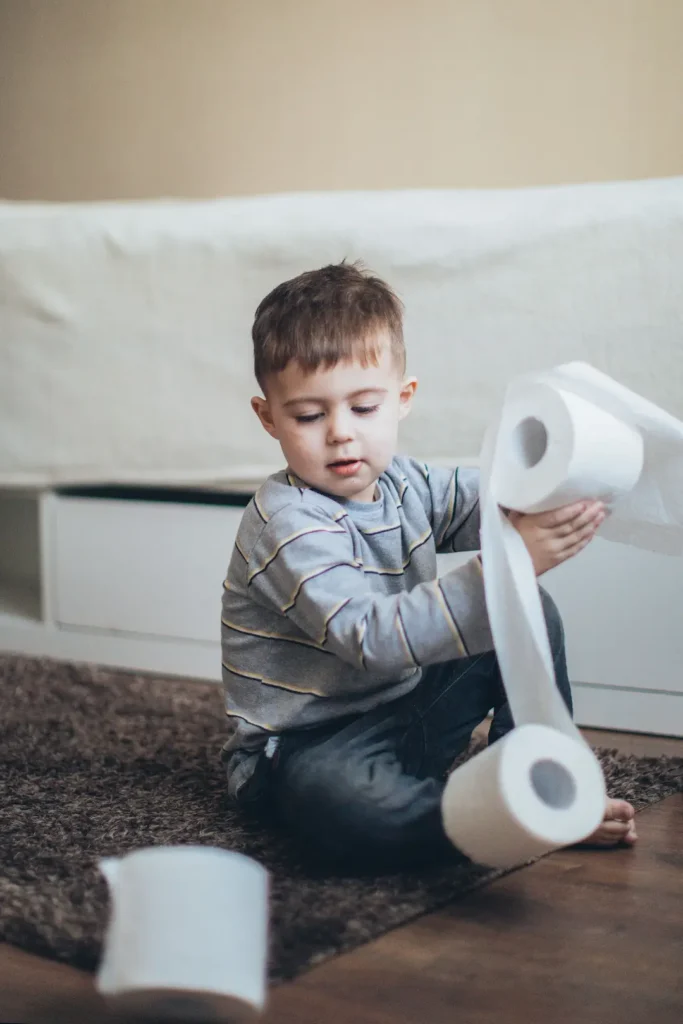 child sitting on the floor indoors unraveling toilet paper. Image complements the blog: how to potty train for daycare guide