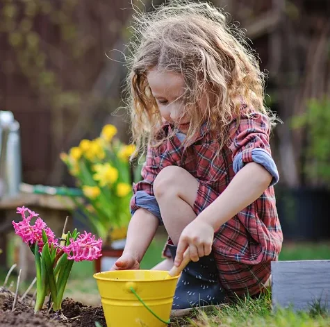 young girl planting flowers, highlighting preschool nature activities, nature activities for kids, nature lesson plans for preschoolers, nature activities for preschoolers, nature preschool activities.