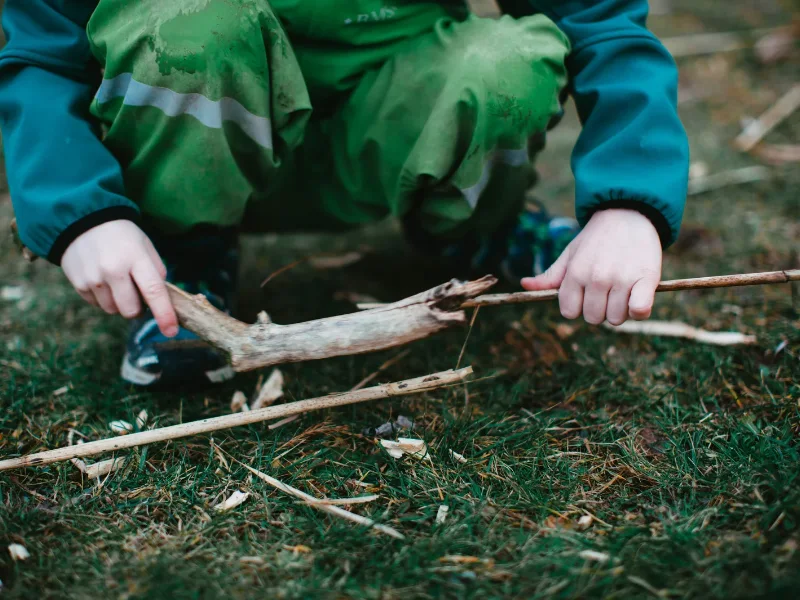 a boy stacks sticks to build a nature structure as part of an outdoor stem activities