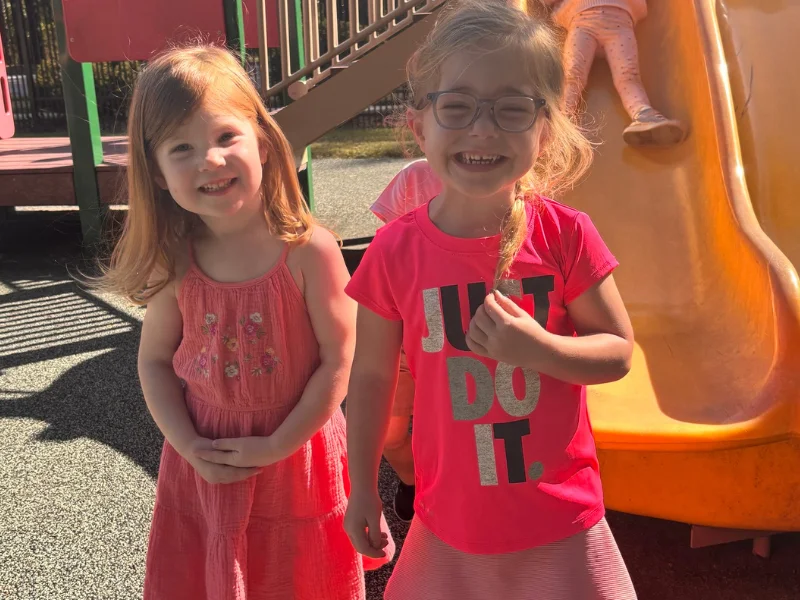 Two female preschoolers smiling. Image accompanies the blog titled, "Your Ultimate Preschool Tour Checklist."